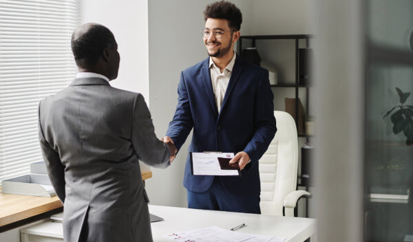 Specialist of visa center congratulating man of getting visa, they standing and shaking hands