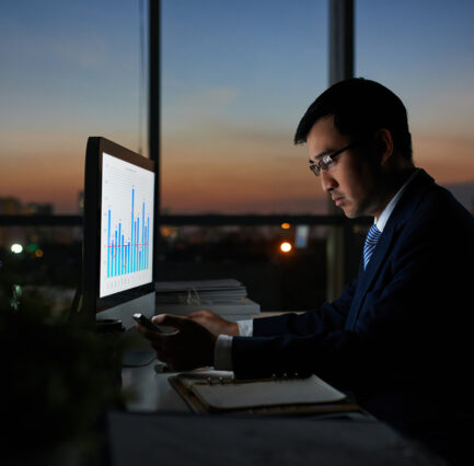 Serious Vietnamese businessman working on financial report in dark office